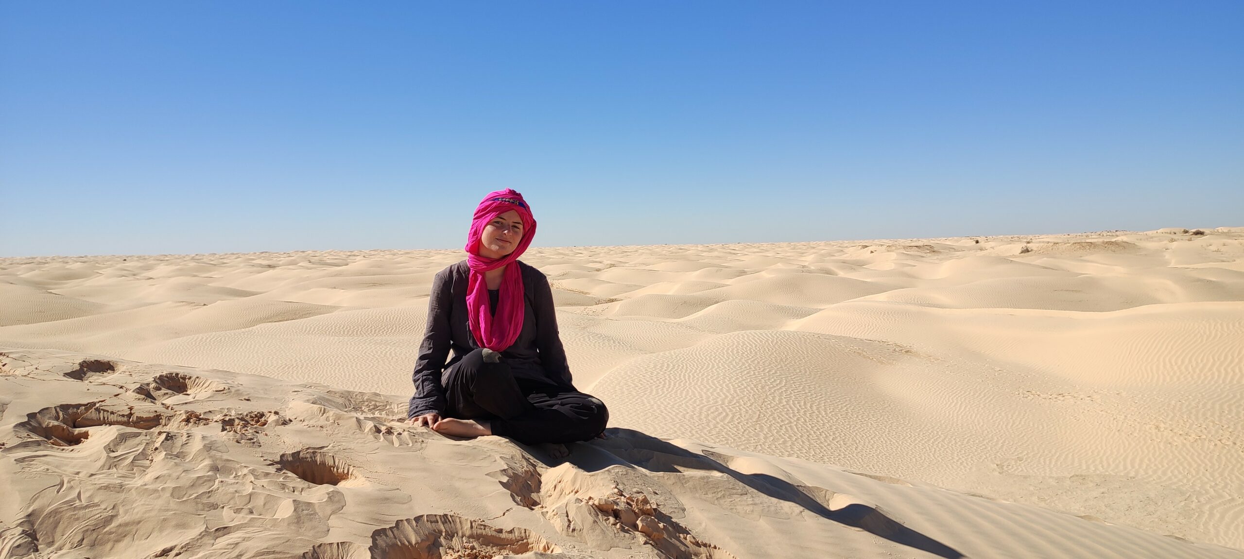 Photo de Laure Beuget assise sur une dune marquée par des pas.